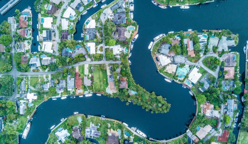 Drone image of a neighborhood in Fort Lauderdale, Florida. A winding river runs through the neighborhood. Homes have dock and boat access to the water.