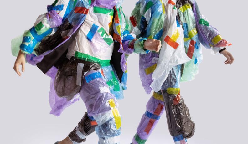 A man and a woman strutting wearing multicolored plastic clothes.