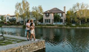 Two women stand with their arms around a young girl, their daughter, at the edge of a small lake with homes and trees in the background. Clean energy for all.