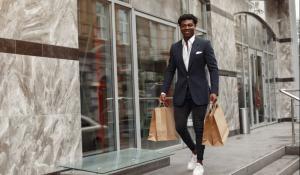 black man in suit walking with paper bags in hand. 