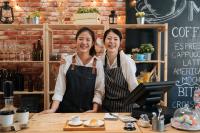 mother and daughter wearing aprons and smiling. They are coffee shop owners ready to make coffee.