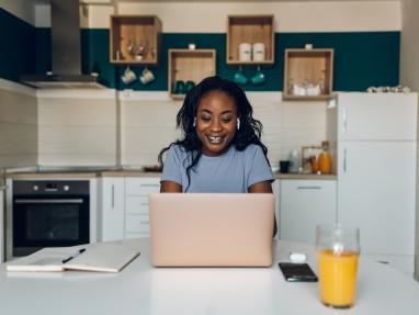 A young Black woman looks for financial information on her laptop in her kitchen