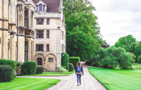 Back of a college student with a book bag walking next to a school building, greening your dorm is the new thing