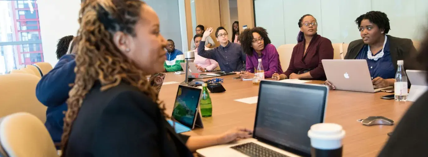 many women sitting around a conference table in an office setting. They appear to be discussing. 