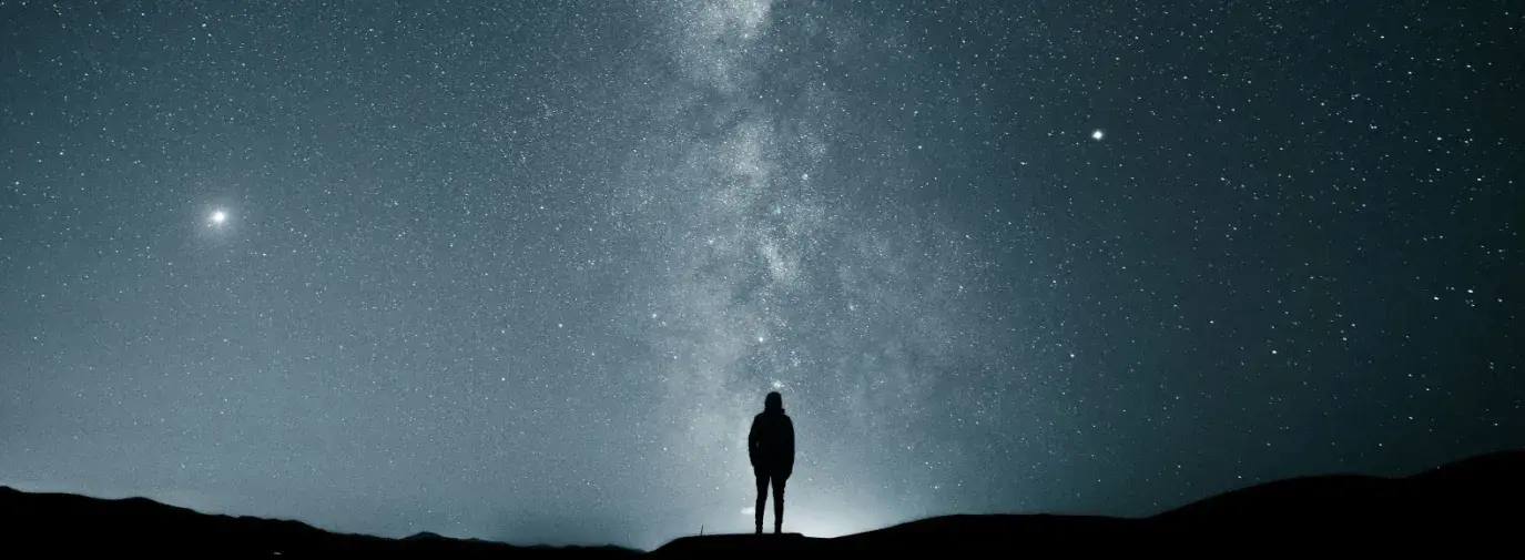the silhouette of a person in the dark, looking up at the milky way.