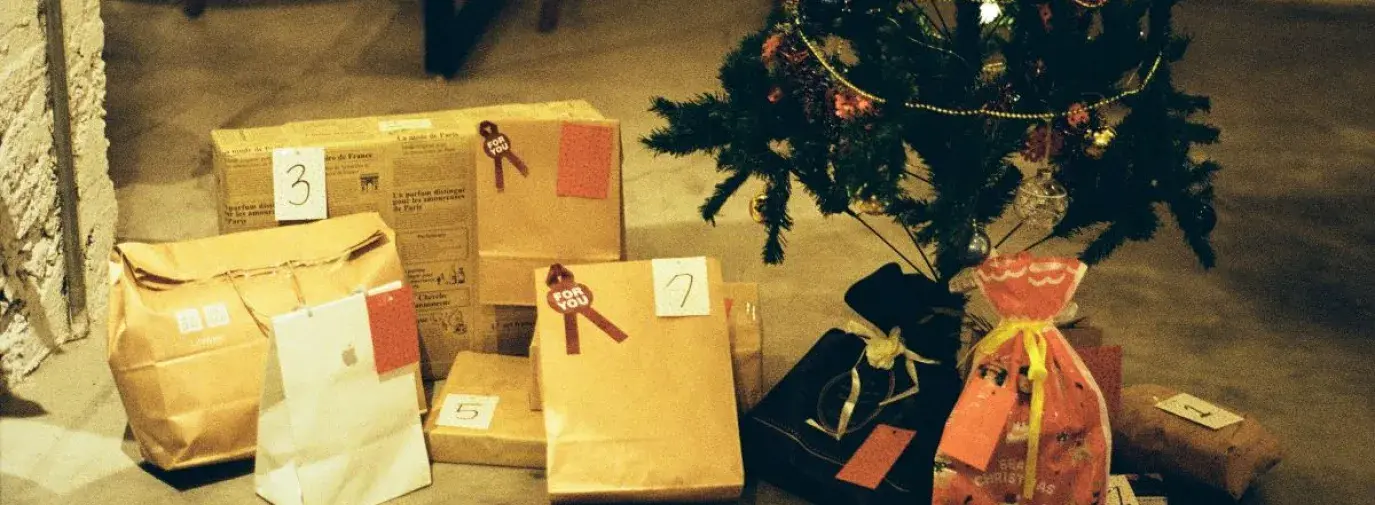 gifts wrapped in brown paper bags and cloth bags under a small christmas tree