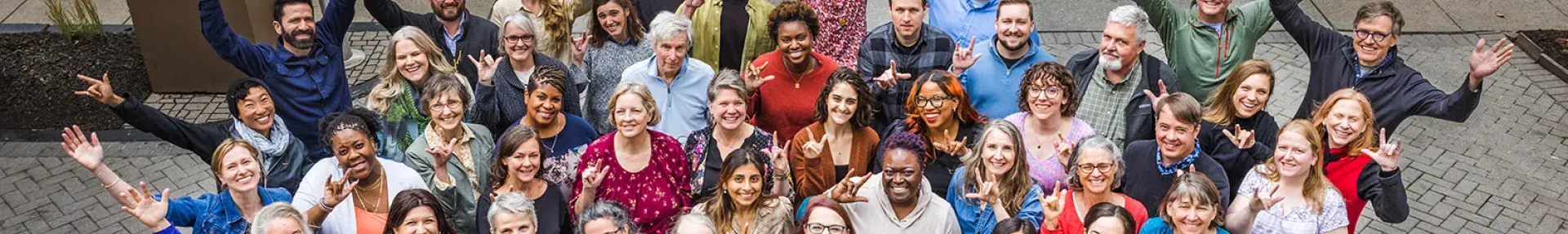 the Green America staff and Board grouped together smiling at the camera. Everyone is doing the ASL sign for I love you. 