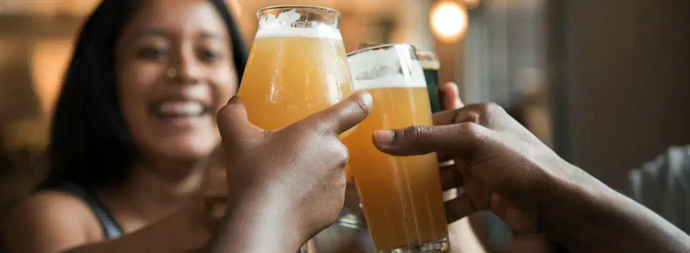 Friends toasting with craft beer glasses in a warm, social setting.