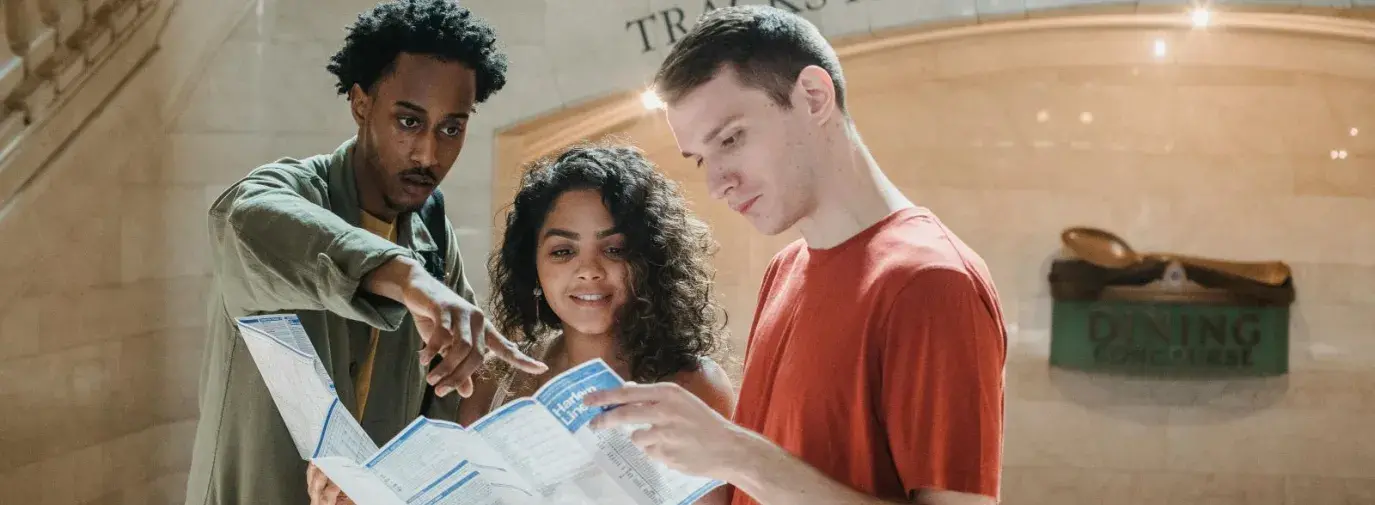 three young people looking at a train station times table.